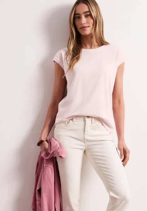 Frau in rosafarbenem T-Shirt und heller Hose, hält eine rosa Jacke
